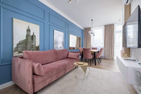 A stylish living room featuring a pink sofa, blue accent wall with artwork, and natural light streaming in through large windows.

