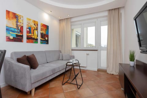 A cozy living room with a comfortable gray sofa, vibrant wall art, and a large window bringing in natural light.

