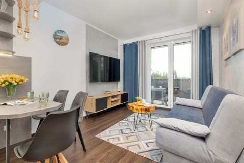 A bright and modern living room featuring a cozy blue sofa, a flat-screen TV, and large windows letting in plenty of natural light.


