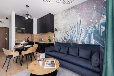 A modern living area featuring a navy sofa and a large botanical mural in soft pink, blue, and gray tones. A round wooden coffee table ties the seating space together.
