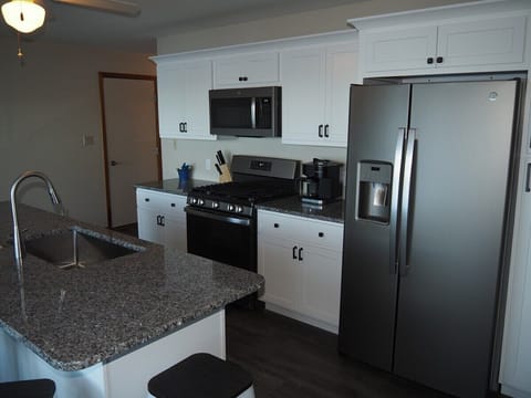 KITCHEN: Newly remodeled and features a gas stove and stovetop, refrigerator, microwave oven, dishwasher, Keurig coffee maker, toaster, island with sink, barstools, lots of counter space and cabinets, and a good supply of cooking & dining utensils.