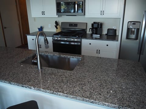 KITCHEN: Newly remodeled and features a gas stove and stovetop, refrigerator, microwave oven, dishwasher, Keurig coffee maker, toaster, island with sink, barstools, lots of counter space and cabinets, and a good supply of cooking & dining utensils.