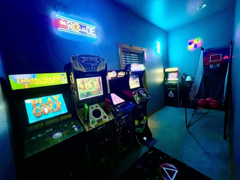 Arcade room illuminated by neon signs with classic game cabinets and a basketball shooting game.