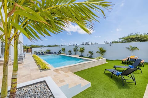 A serene tropical oasis featuring a private pool bordered by lush palms, inviting loungers on manicured grass, and a shaded dining spot—your perfect retreat under sunny skies.