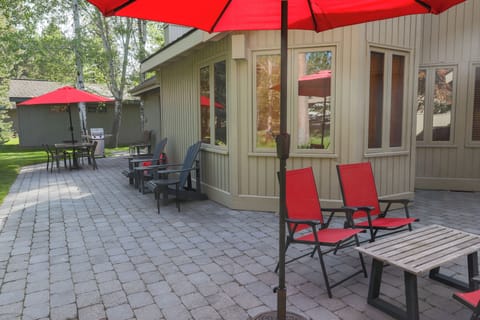 Your private patio invites lazy afternoons lounging on comfortable chairs, sipping drinks under bright red umbrellas, with lush greenery surrounding your peaceful retreat.