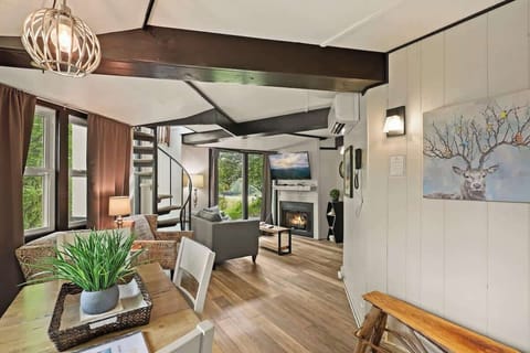 Captivating dining space with a warmly lit, neatly decorated square table and white chairs. A glimpse of the living space, complemented by a striking deer portrait painting, adds to the inviting ambiance