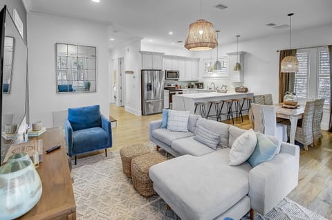 Open Living & Dining Space - Step into the cozy living area of Surf on Turf—a retreat adorned with a gourmet kitchen, dining room area, sectional sofa, two armchairs, and a large TV -- creating the perfect setting for entertaining.