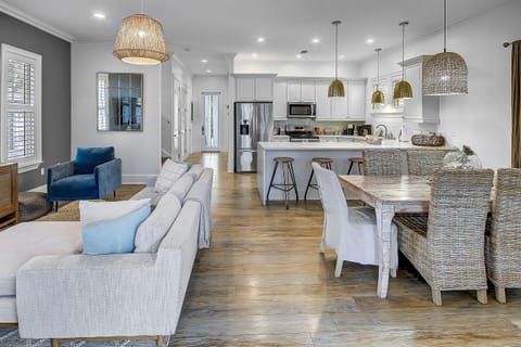 Open Living & Dining Space - Step into the cozy living area of Surf on Turf—a retreat adorned with a gourmet kitchen, dining room area, sectional sofa, two armchairs, and a large TV -- creating the perfect setting for entertaining.