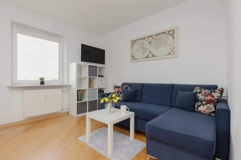 A bright living room with a blue sectional sofa, a white coffee table, and a decorative wall art piece, creating a cozy and functional space.

