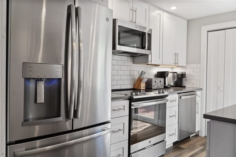 The fully equipped kitchen features a crisp and modern look with all white cabinets, light gray countertops, and stainless steel appliances.
