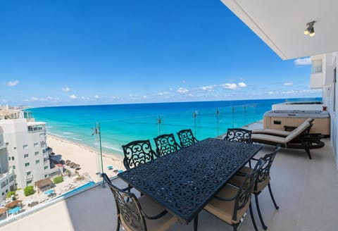 Penthouse 1 of 5: Penthouse 3703 Terrace has a hot tub. This is 1 of 5 penthouses in this combination. Balcony with ornate black metal dining set, cushioned lounge chairs, wood-paneled hot tub, and glass railing overlooking turquoise ocean.