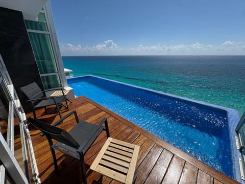 Private terrace with teak decking, two black mesh chairs, and an infinity pool overlooking the ocean.