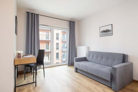 A bright living area with a gray sofa, a small wooden table, and a large window letting in natural light, offering a cozy and inviting space.
