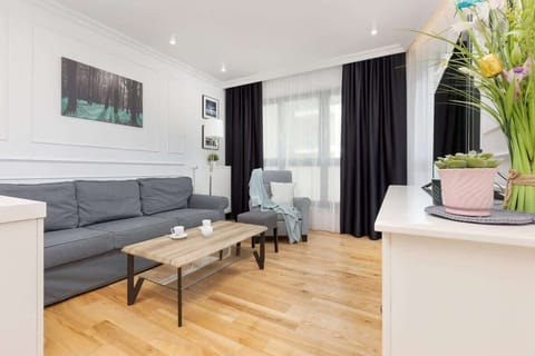 A bright living area featuring a gray sofa, a white coffee table, and large windows with curtains, creating a cozy and inviting space.
