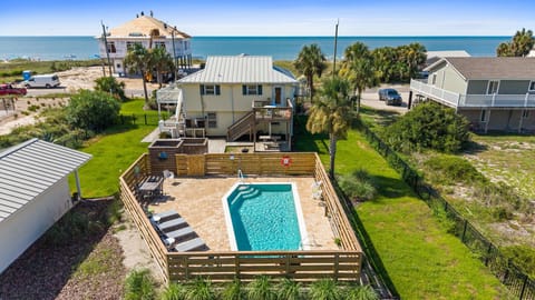 Aerial view of a beachside vacation home featuring a private swimming pool, outdoor lounging spaces, and direct access to pristine coastal surroundings just steps from the shore.