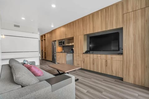 The bright living room features a couch, a 55” TV, a large floor mirror, a coffee table, and built-in shelving for additional storage space.