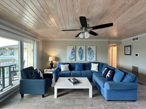 Unwind in your coastal-inspired living room with plush blue sectional seating, natural wood ceiling, and peaceful water views.