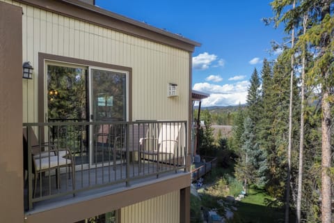 Modern mountain retreat with elevated deck overlooking forested valley and distant peaks under clear blue skies.