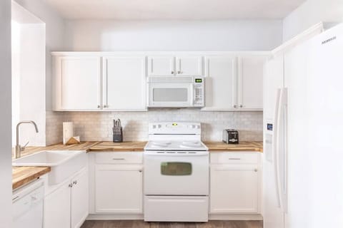 The clean white appliances are broken up with a tumbled marble backsplash and sealed customized butcher block countertops and an apron sink. 