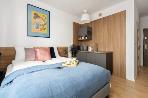 A cozy bedroom with a double bed, soft blue bedding, and a colorful wall painting, creating a vibrant yet relaxing space.
