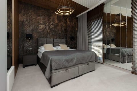 A stylish bedroom with a double bed, gray bedding, and decorative wallpaper, complemented by warm lighting and modern furniture.
