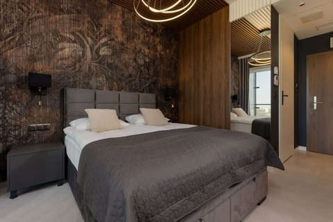 A stylish bedroom featuring a double bed with gray bedding, decorative wallpaper, and a modern chandelier, creating a luxurious atmosphere.
