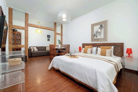 A spacious bedroom area with a large bed and a dining set in the background. Wooden beams and floors give the room a rustic charm.