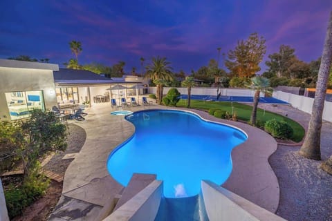 The illuminated pool and spacious backyard framed by palm trees create an inviting oasis for evening relaxation under a stunning twilight sky.