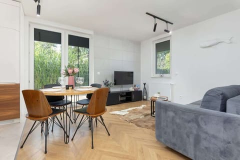 A modern open-plan dining and living area featuring wooden floors, a stylish wooden dining table, and a cozy gray couch.