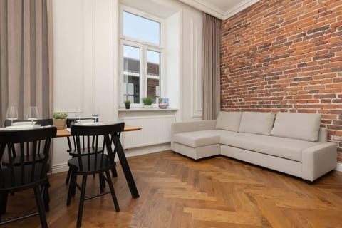 A cozy living room featuring a brick accent wall, white curtains, a gray sectional sofa, and a black dining table with chairs.
