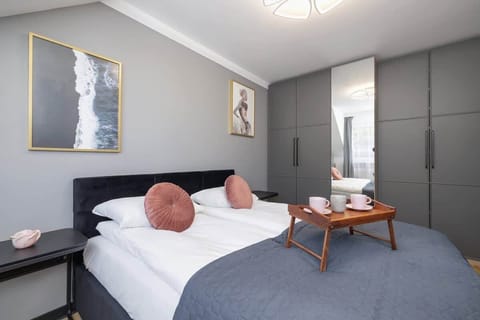 A modern attic bedroom with twin beds, gray walls, skylights, and minimalist decor including framed wall art.