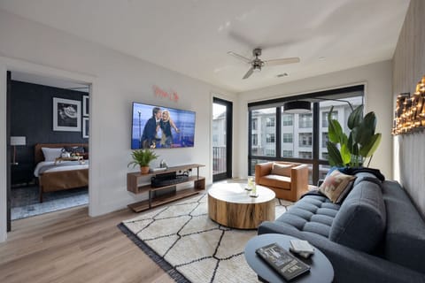 Modern open concept living area with floor to ceiling windows, designer furniture, smart TV, and access to private patio.