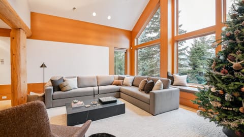 - Bright living area with panoramic forest views through floor-to-ceiling windows  
- Spacious sectional sofa ideal for relaxing after a day on the slopes  
- Warm wood accents and natural light create a cozy mountain retreat 