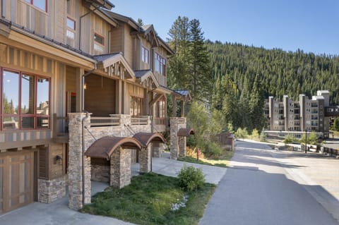 Rustic mountain townhomes with stone pillars and copper awnings nestled by forested hills.