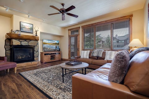 Cozy up in your spacious living room featuring plush leather seating, crackling stone fireplace, and mountain views through wooden blinds.