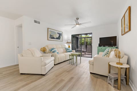 Beautifully decorated living room is equipped with a smart TV, a comfy leather sofa sleeper, a loveseat, a cozy chair, and sliders to a screened patio.