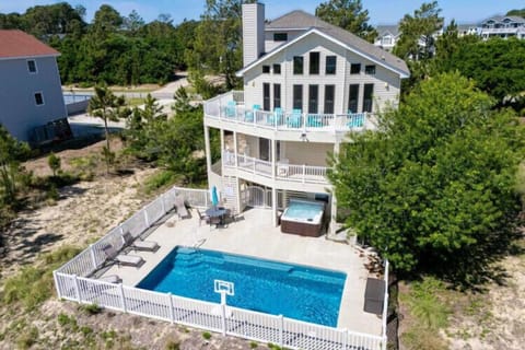 Aerial perspective showing a spacious beachside rental with private pool, hot tub, and multiple balconies surrounded by coastal greenery—a serene retreat near the shore.