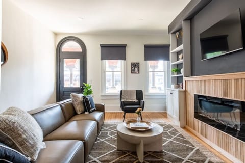 Living room with a leather sofa, a round coffee table, a black armchair, a wall-mounted TV, and a modern fireplace