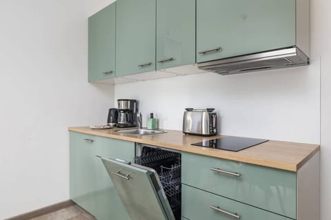 A minimalist kitchen with pastel green cabinets, wooden countertops, and modern appliances.

