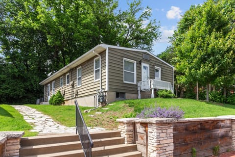 Welcoming front exterior of the duplex with a stone walkway, mature trees, a landscaped retaining wall, and steps from the street.