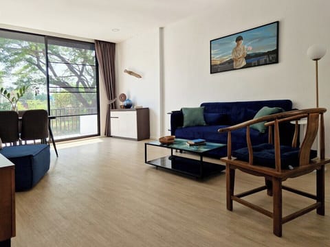 Enjoy a spacious and sunlit living room with floor-to-ceiling windows overlooking lush greenery. The comfy blue sofa, modern decor, and peaceful vibe make it a perfect spot to relax, sip coffee, or plan your day's adventures in Chiang Mai!