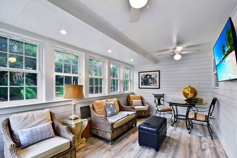 Sun Porch with TV and Wicker Seating - Wicker seating, ceiling fan, wide windows, and wall-mounted TV in the sun porch.