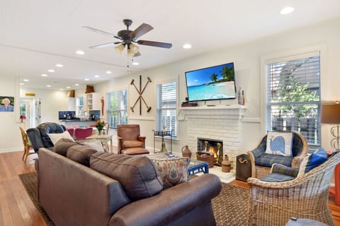 Living Room With Fireplace And Smart TV - Main gathering space with a white brick fireplace, mounted TV, leather seating, and an open path to the kitchen and dining room.