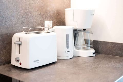A close-up of small kitchen appliances, including a toaster, coffee maker, and blender, neatly arranged on a countertop.

