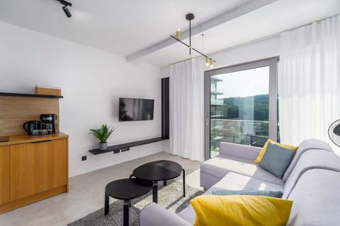 A view of the living space with a large window, a mounted TV, and the gray sofa with colorful accents.
