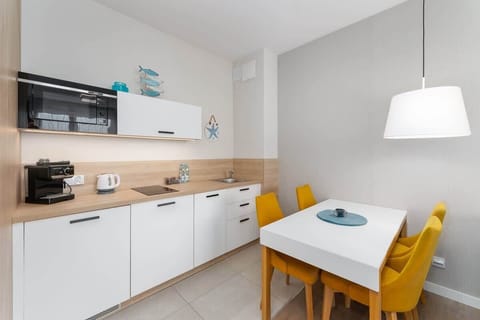 A sleek kitchen with white cabinetry, wooden accents, and a dining area with yellow chairs for a cheerful ambiance.
