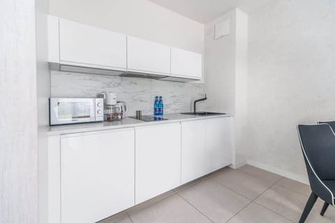 A compact white kitchenette equipped with a microwave, kettle, and storage cabinets, offering modern convenience.

