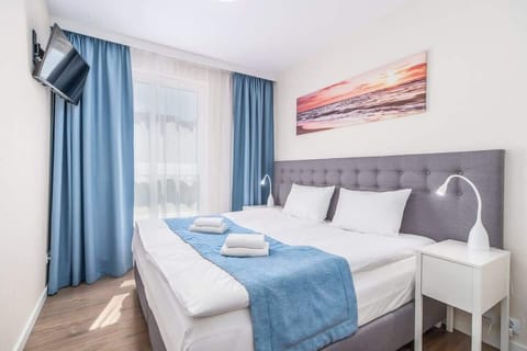 A bright interior combining a gray bed with blue accents, a matching sofa, and large windows dressed in blue curtains.

