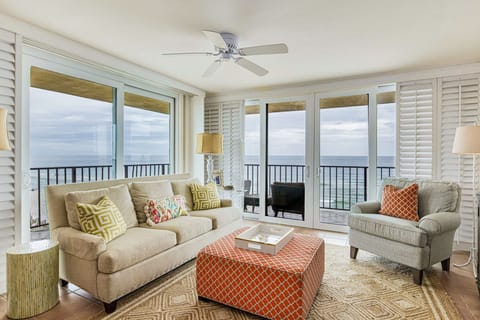 Lei Lani 401's Gulf-view living room — open-concept layout with coastal décor, sofa, coral ottoman, ceiling fan, and sliding glass doors opening directly to the Orange Beach balcony.