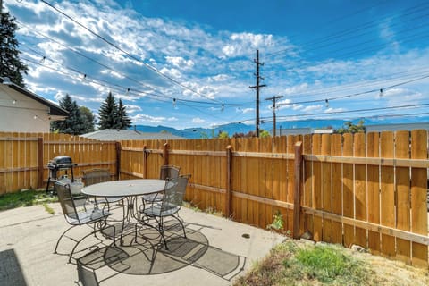 Private patio with a round outdoor table and metal chairs, strung with overhead lights and framed by a wooden fence. Fire up the nearby grill and enjoy easy outdoor meals while taking in the open sky and distant mountain views beyond the yard.